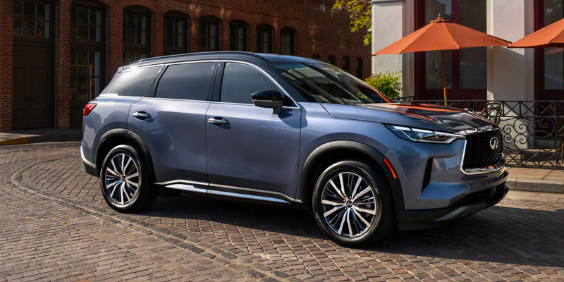 Passenger side view of a blue 2025 INFINITI QX60 parked on a brick city street