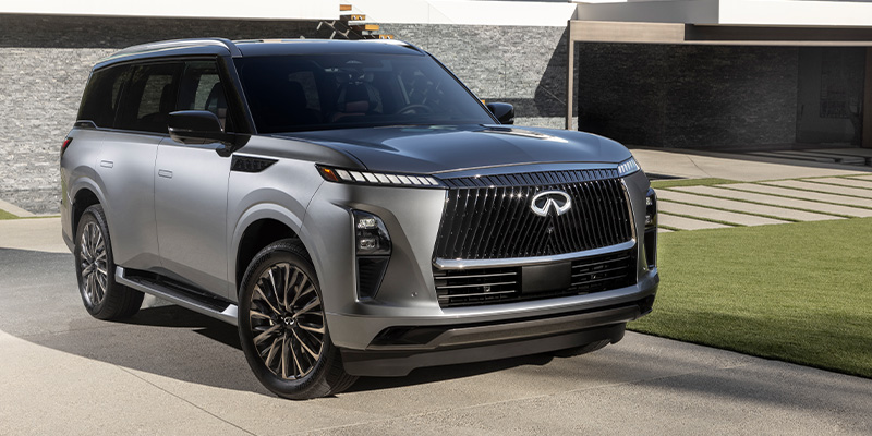 A sleek silver 2025 Infiniti QX80 SUV parked in front of a modern building with a luxurious design
