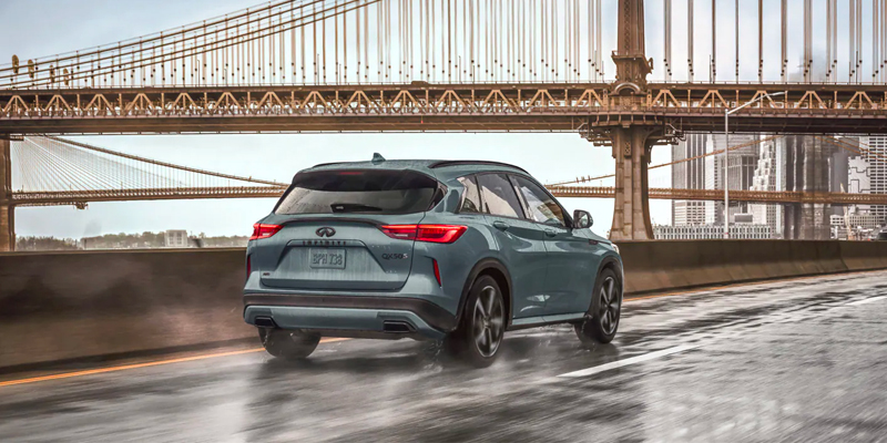 The image shows a 2025 INFINITI QX50 driving on a rain-soaked road.